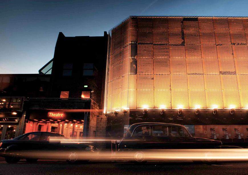 Long exposure photo of car passing the Young Vic box office and Main House at dusk with the light trail from the headlights clearly visible.