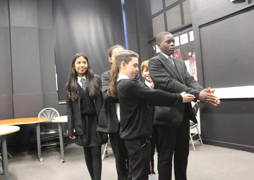 4 pupils in school uniform in black wall theatre room, engaging in a group activity