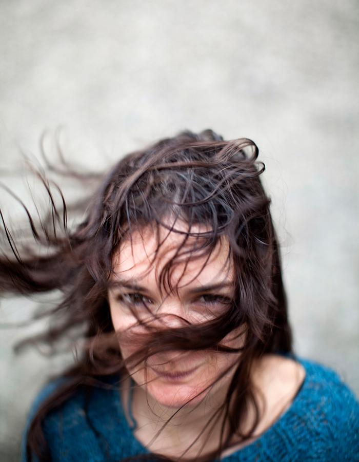 brunette women in a blue top with the wind blowing in here face that half of her face is covered.